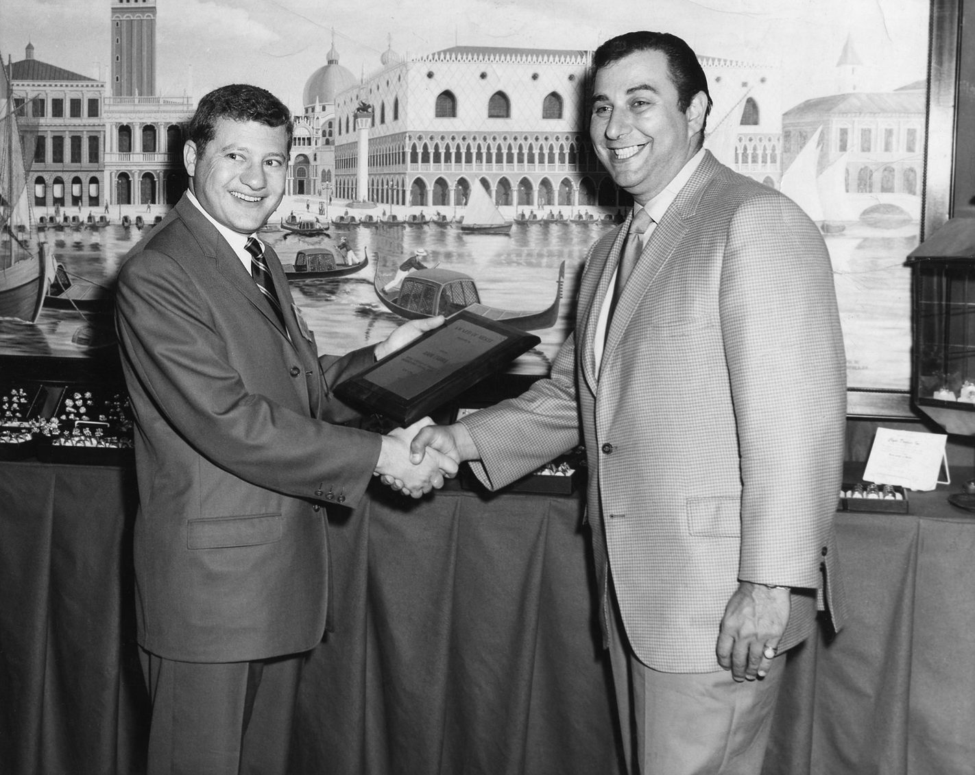 Two men shaking hands over an award of merit